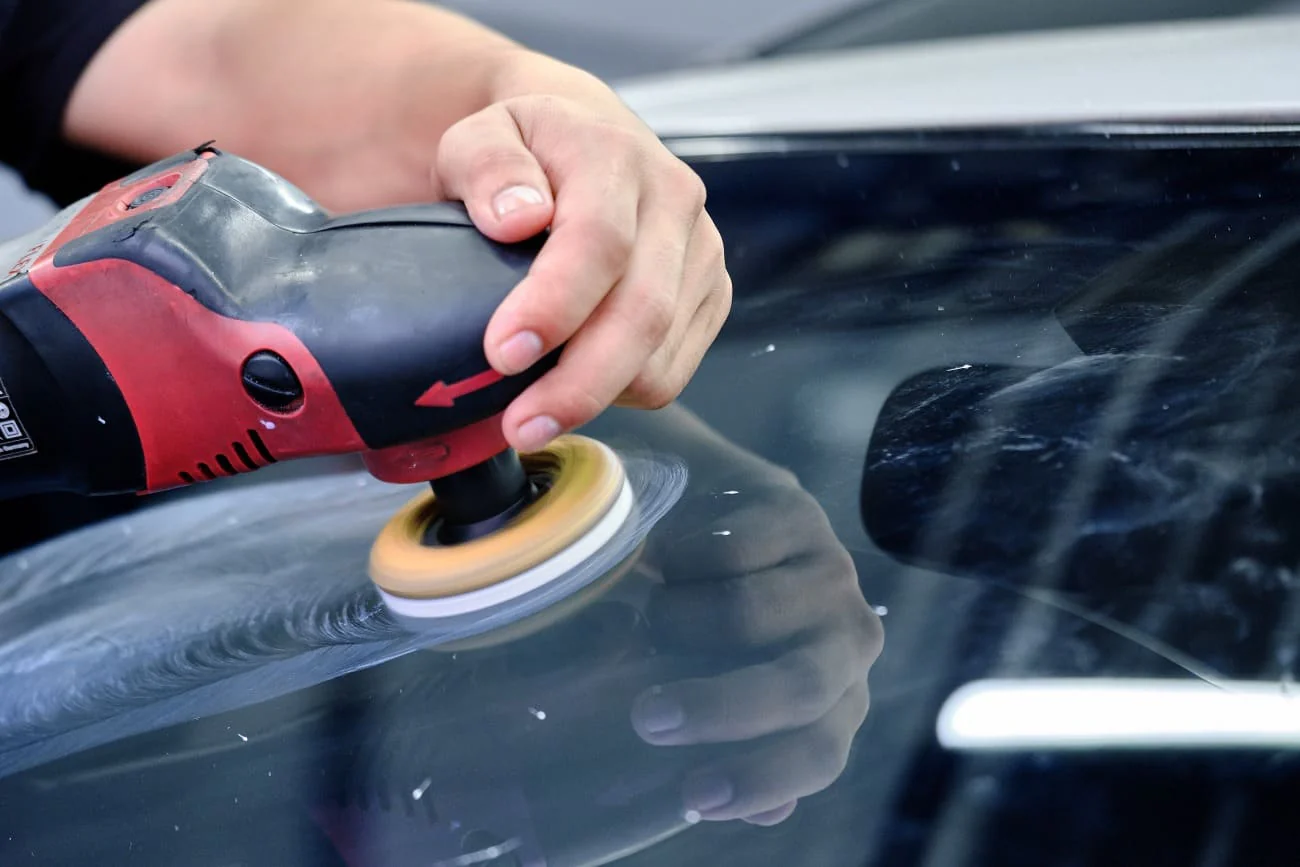 Technician polishing auto glass with a variable-speed machine polisher