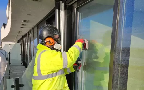 Technician in safety gear polishing commercial storefront glass on-site